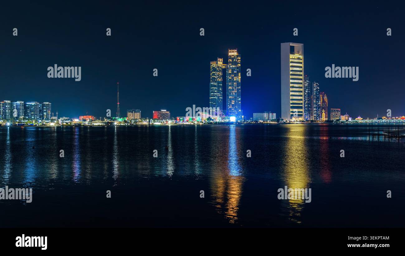 Abu Dhabi, Emirati Arabi Uniti - 27 novembre 2025: Sede centrale ADNOC con Etihad Towers riflessa sul lungomare di Abu Dhabi Corniche di notte, complesso di intrattenimento i Foto Stock