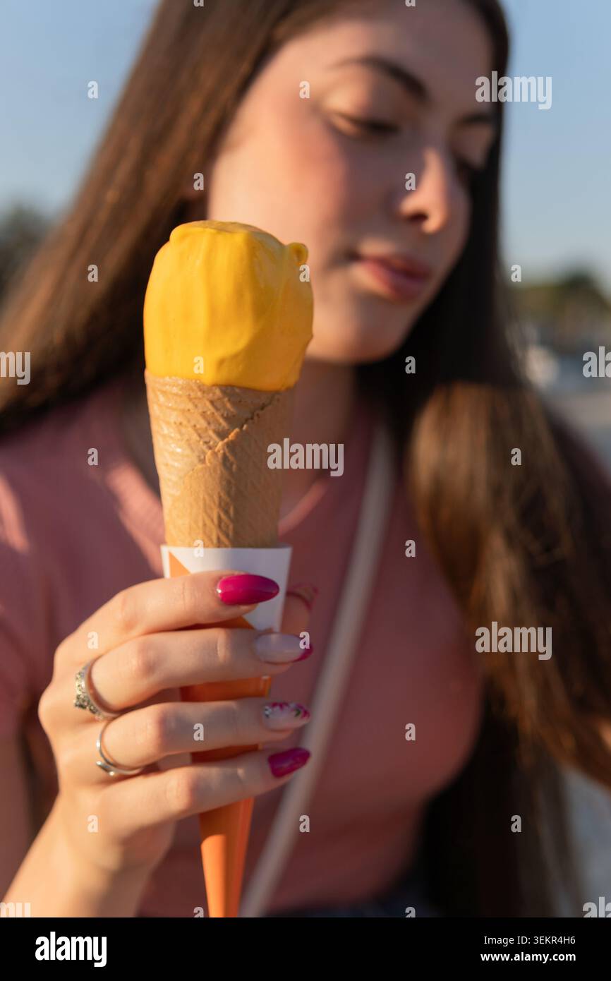 Una donna che tiene un cono di gelato. Indossa una camicia rosa e ha i capelli lunghi Foto Stock