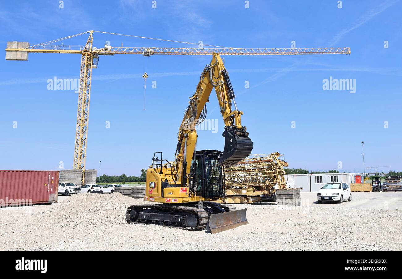 Pavia di Udine, Italia. 30 maggio 2026. Nuovo escavatore cingolato Caterpillar 315 in un cantiere con gru a torre e cielo blu sullo sfondo Foto Stock