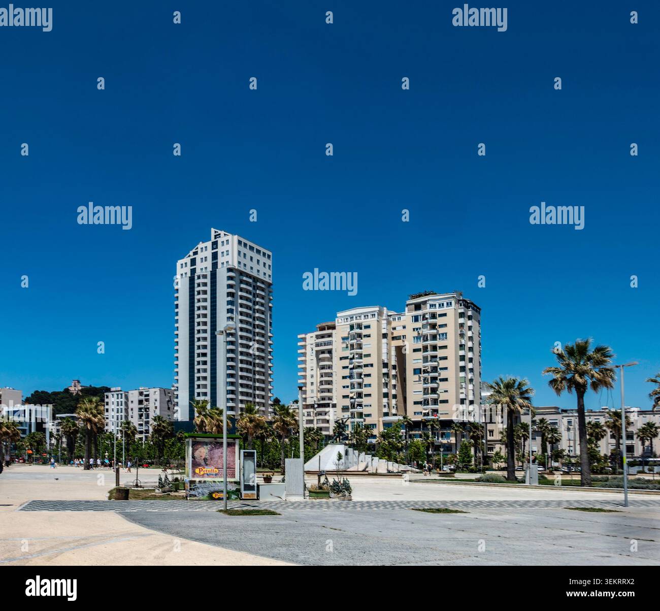 Moderni edifici di appartamenti e palme sorgono lungo un'ampia piazza pubblica sotto un cielo azzurro e limpido a Durazzo, Albania. Foto Stock
