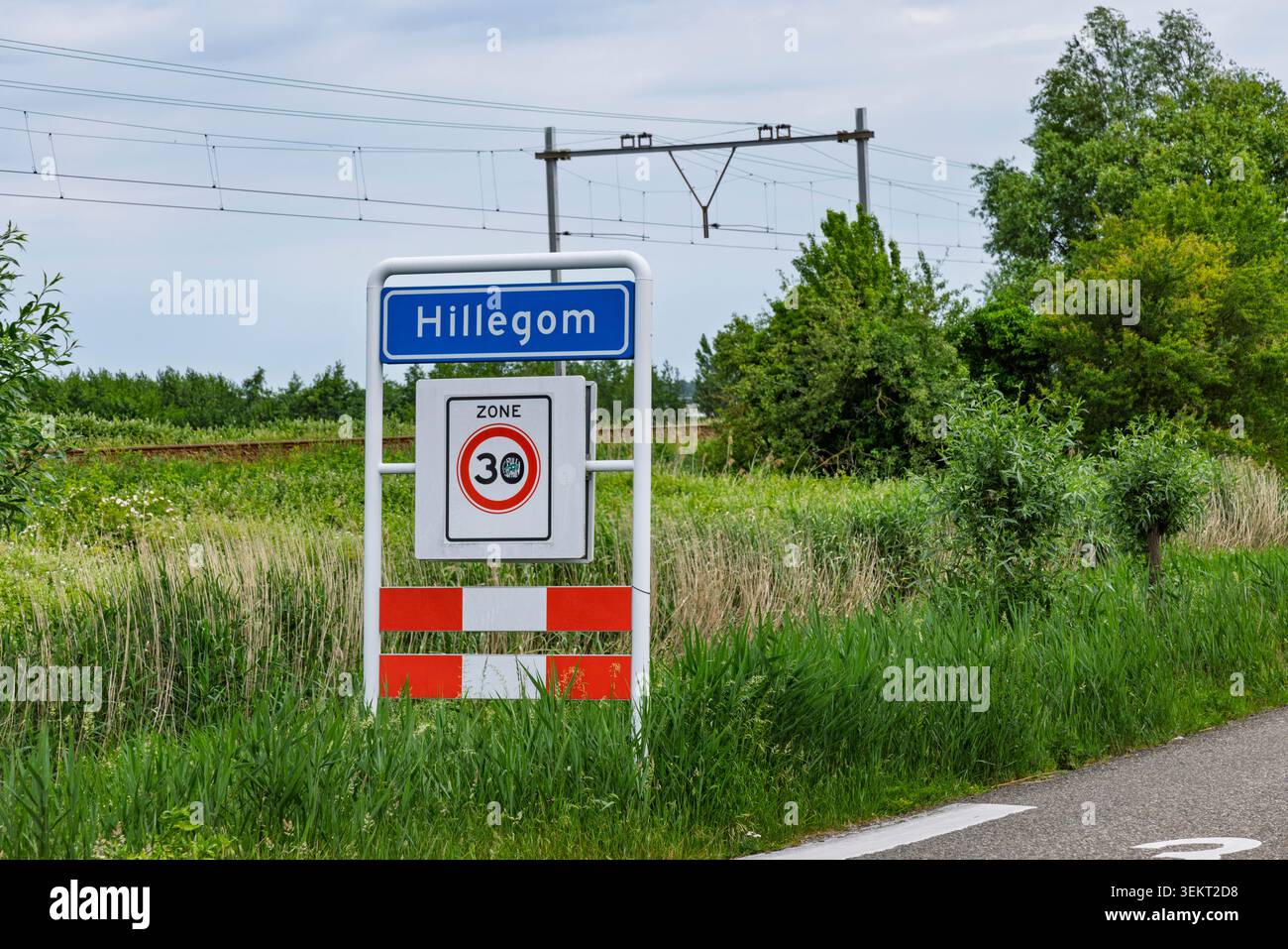Hillegom, Paesi Bassi - 27 maggio 2026 - segnale blu di limite della città di Hillegom con un cartello di limitazione della velocità zona 30 vicino a una linea ferroviaria e a campi verdi. Foto Stock
