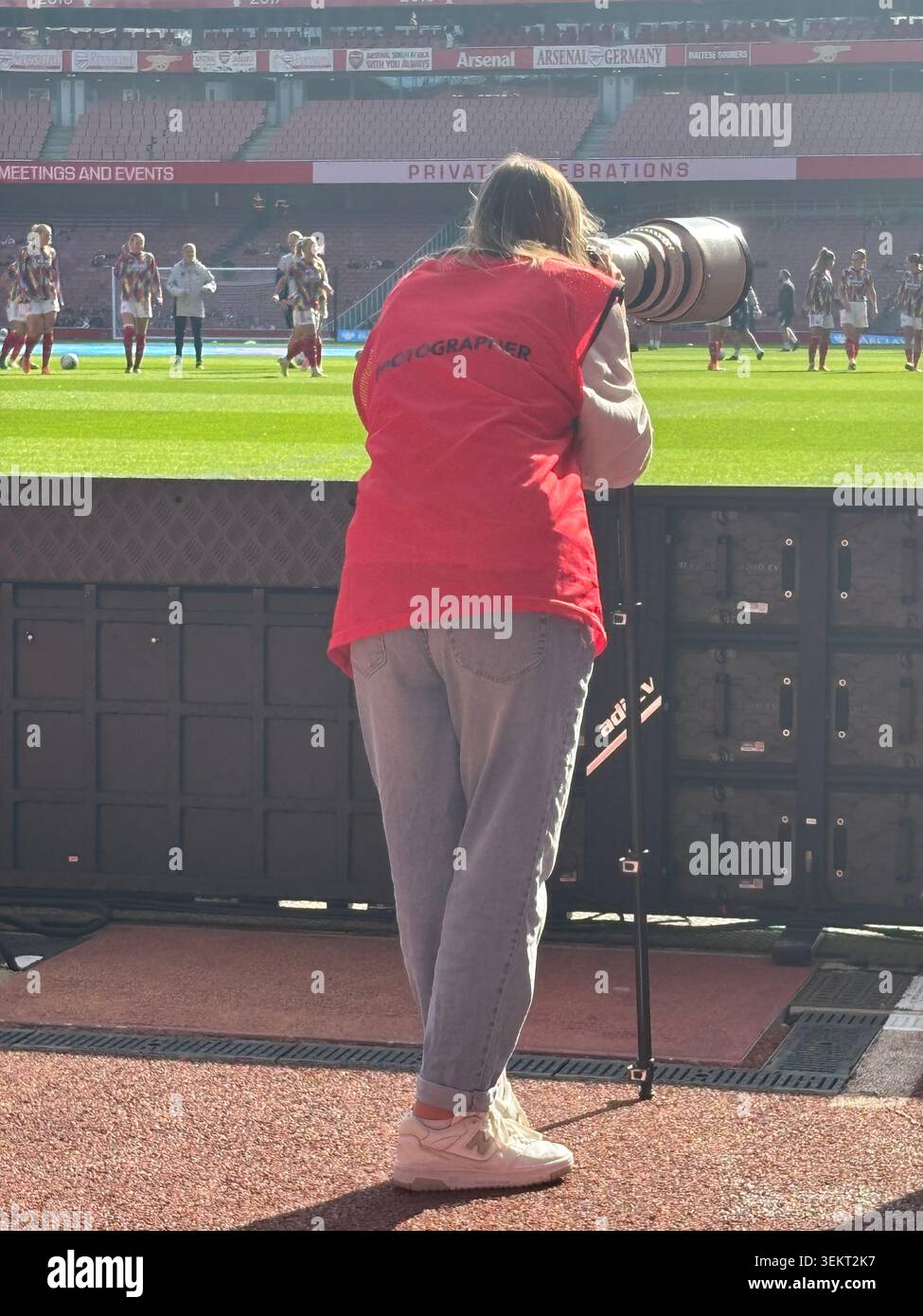 LONDRA UK 12 ottobre Fotografa sportiva femminile in piedi sul campo indossando un giubbotto rosso per i media mentre scatta durante una partita di calcio femminile - Immagine stock catturata con smartphone