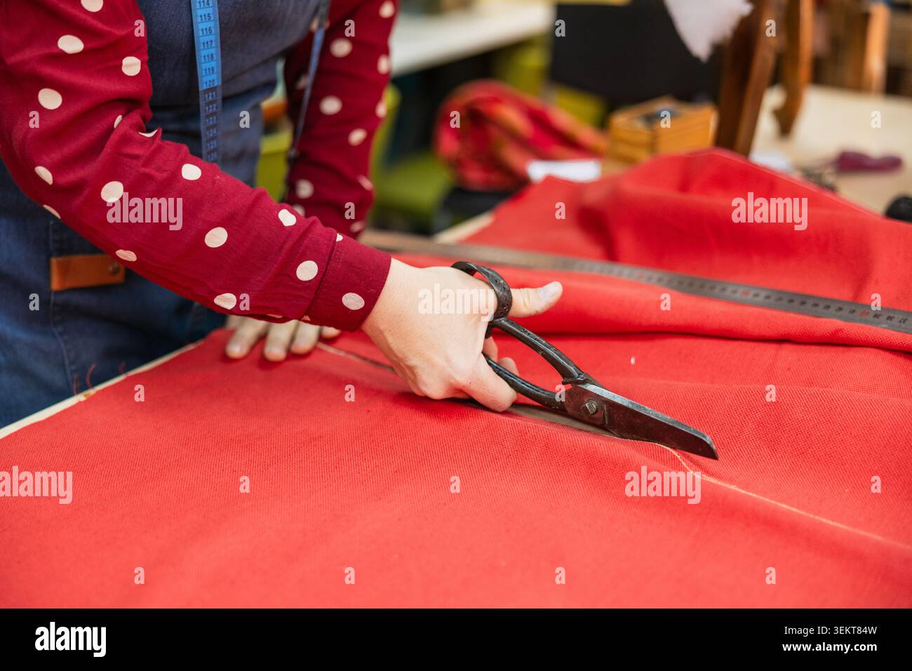 Persona che taglia il tessuto rosso per il processo di tappezzeria Foto Stock