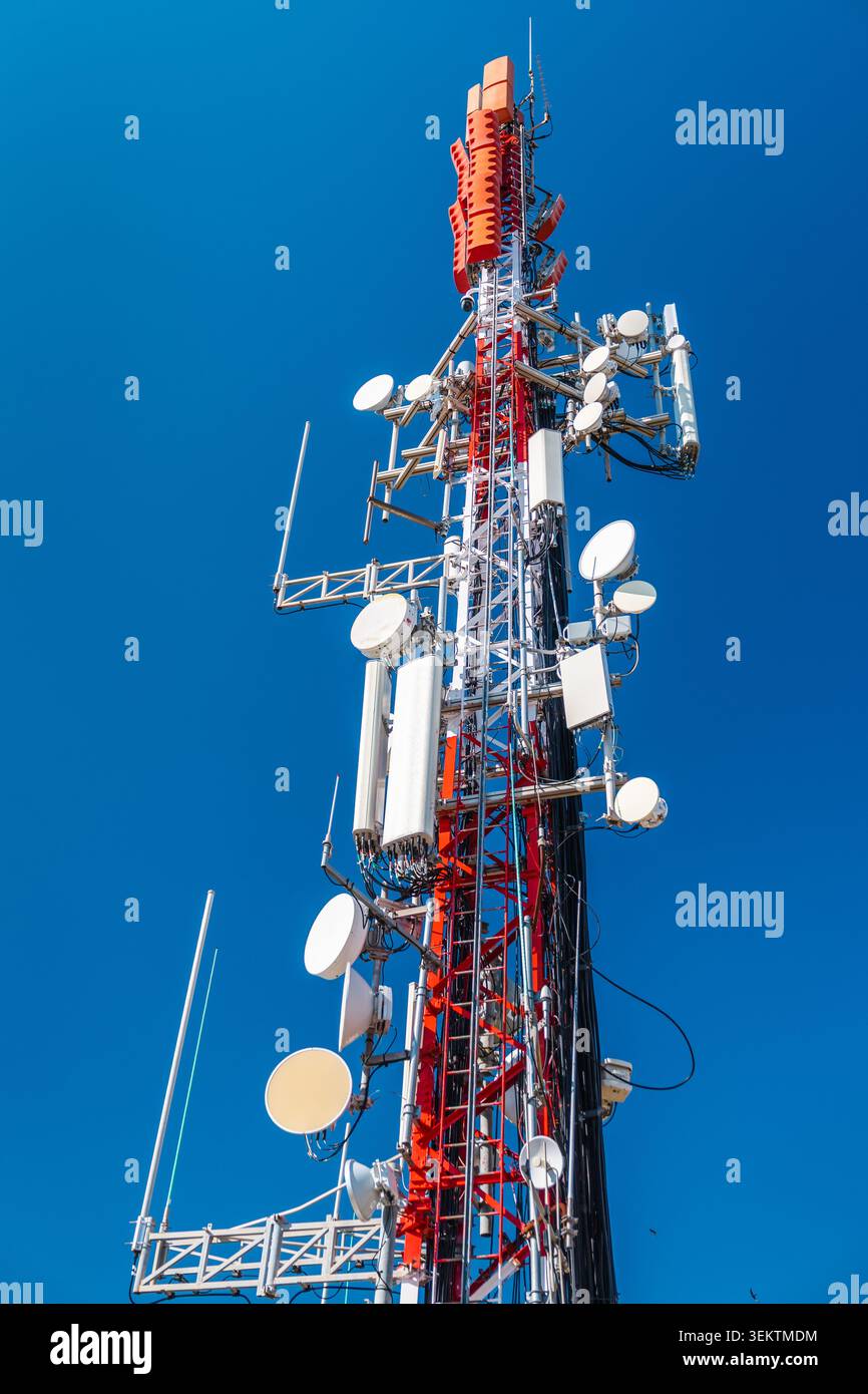 Torre di comunicazione cellulare con più antenne e trasmettitori contro il cielo azzurro Foto Stock