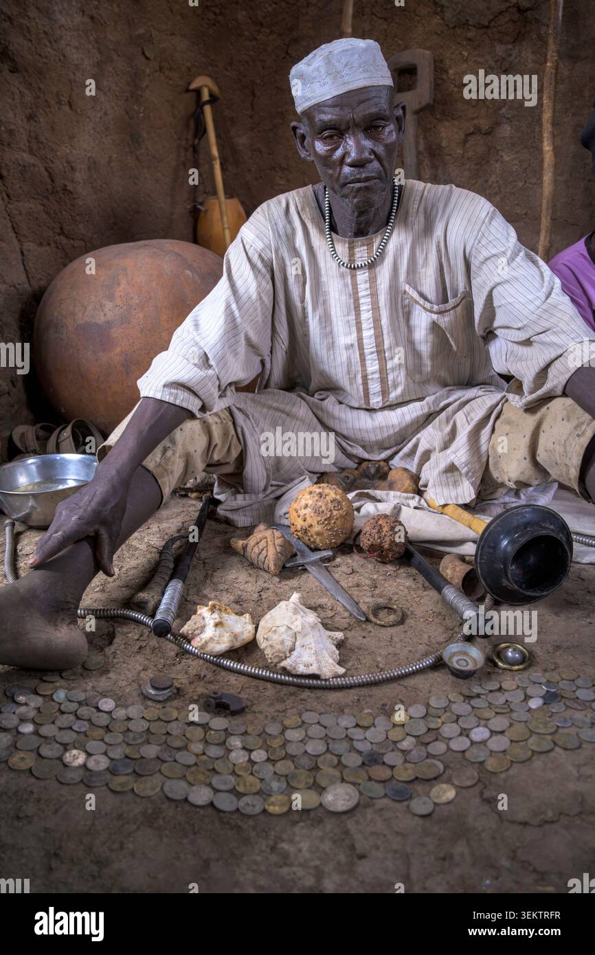 Lo sciamano Nuba Kujur si siede sul pavimento e esegue un rituale curativo. Vari oggetti, tra cui monete e conchiglie, stanno aiutando il processo spirituale. Foto Stock