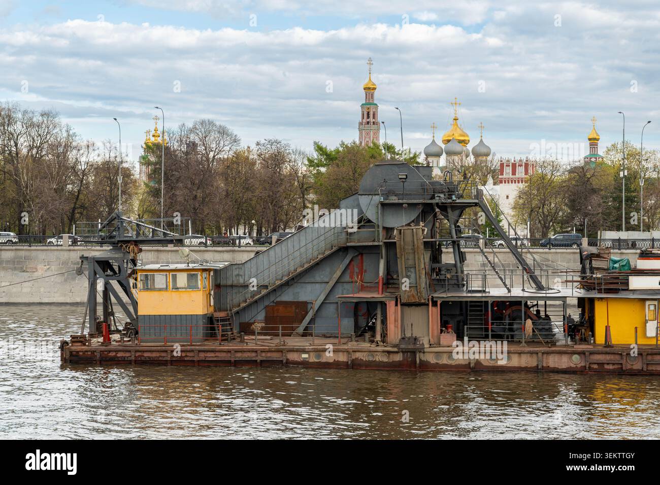 Rusty Dredger Barge che lavora sul fiume, gru pesante e attrezzature per trasportatori sul ponte, scafo industriale con cabina operatore, scena sul lungomare Foto Stock
