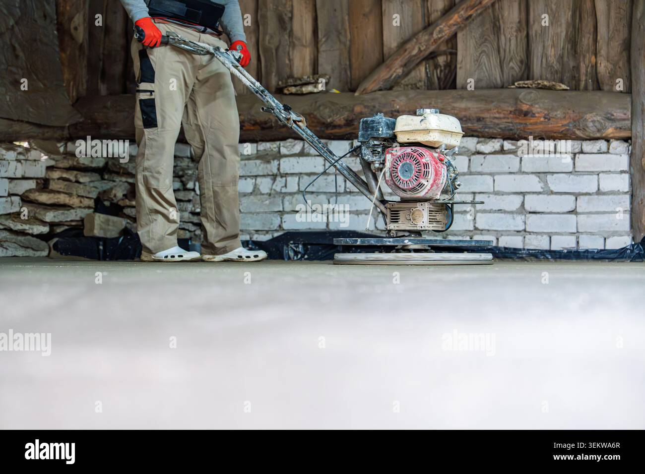 Lavoratore di finitura del calcestruzzo che utilizza una cazzuola elettrica per lisciare la superficie della nuova lastra del pavimento Foto Stock
