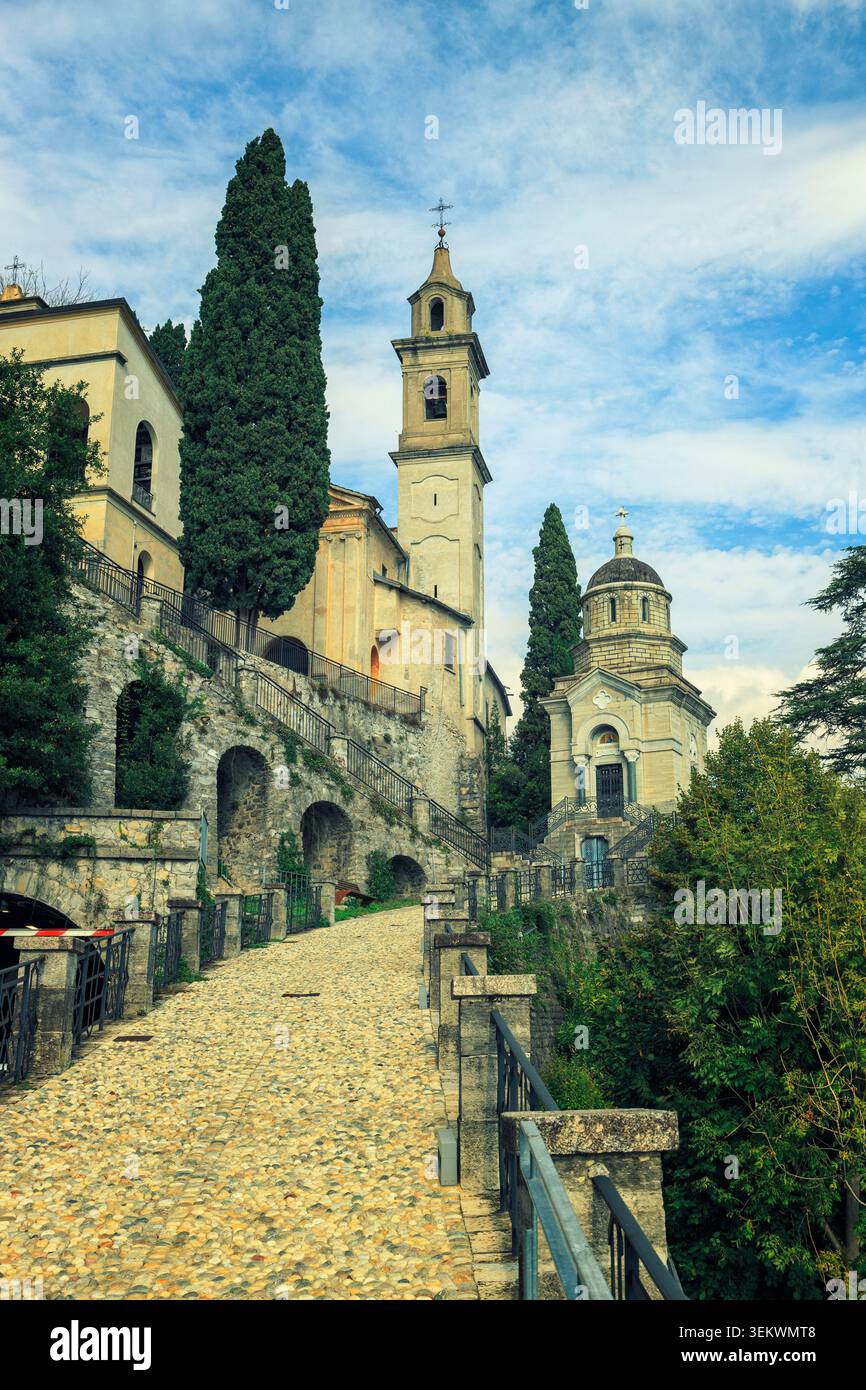 Brienno, Italia - 15.10.2022: Antico complesso religioso caratterizzato da un alto campanile e da una cupola adagiati su un cielo luminoso con vegetazione Foto Stock