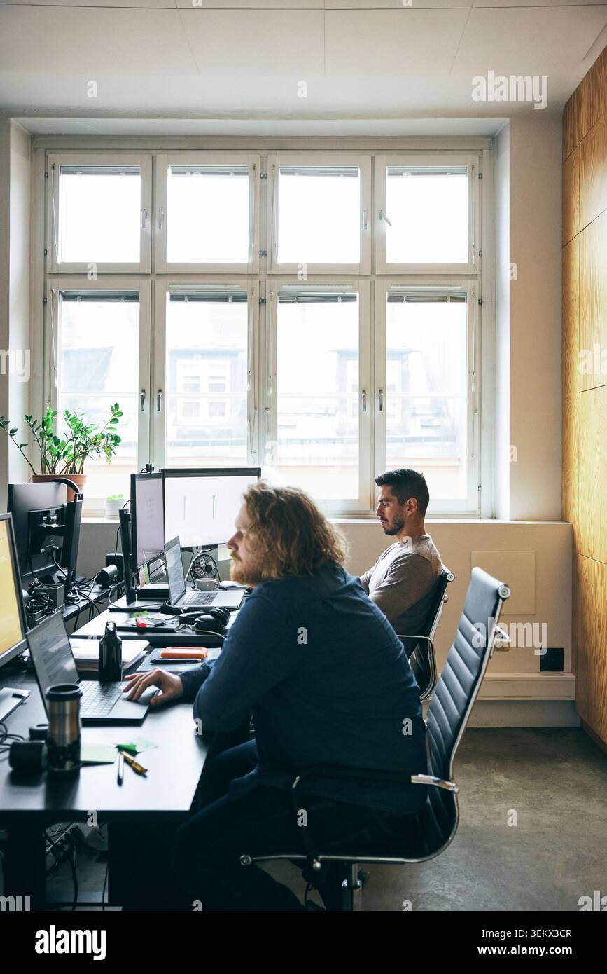 Professionisti maschili concentrati che lavorano sulla tecnologia wireless mentre si trovano in un hub tecnologico Foto Stock