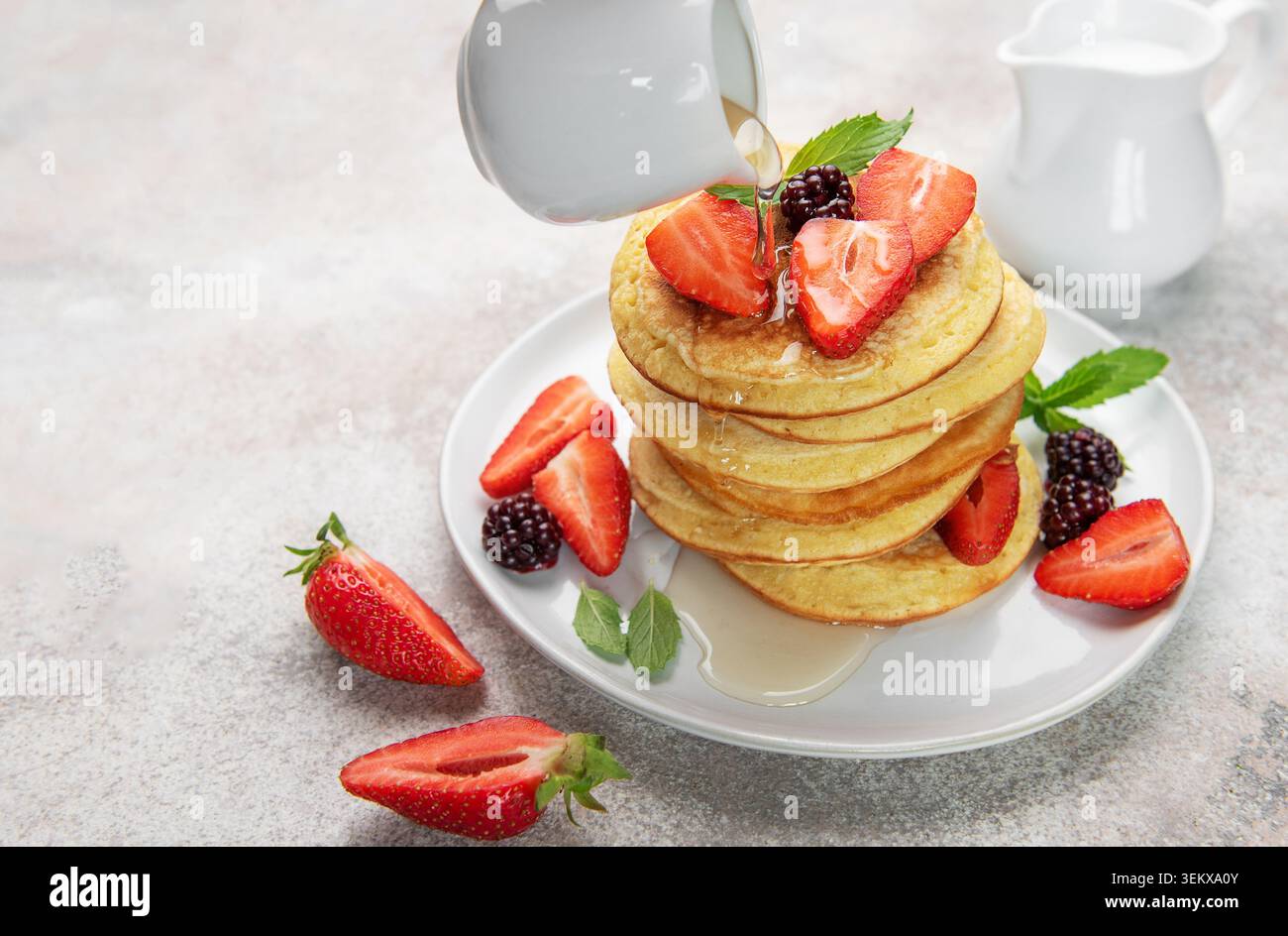 Pila di soffici pancake con fragole fresche, more e menta, condite con sciroppo Foto Stock