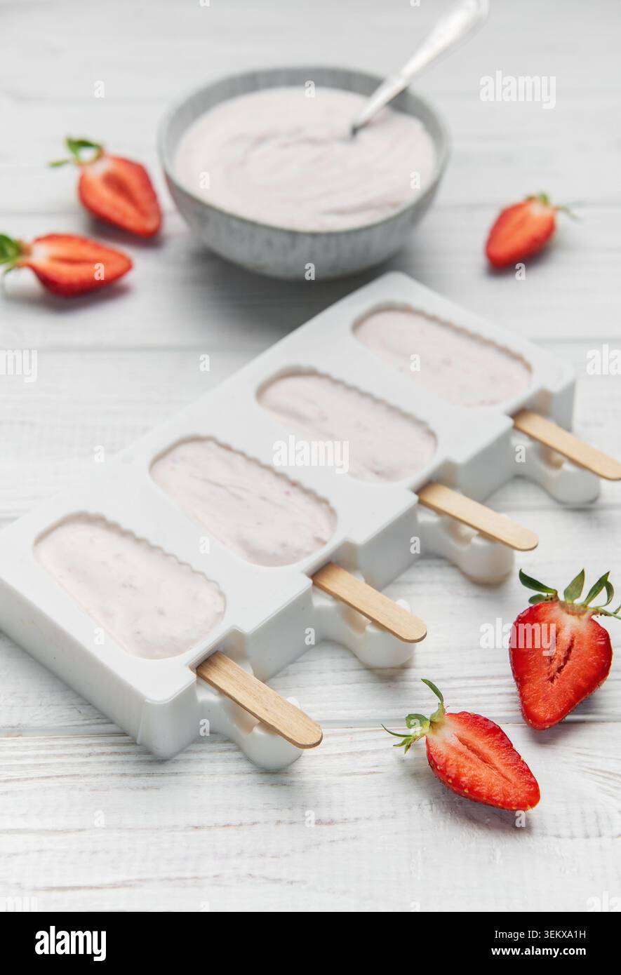 Lo yogurt alla fragola si prepara in muffa con frutti di bosco freschi e cremoso yogurt su un tavolo di legno Foto Stock