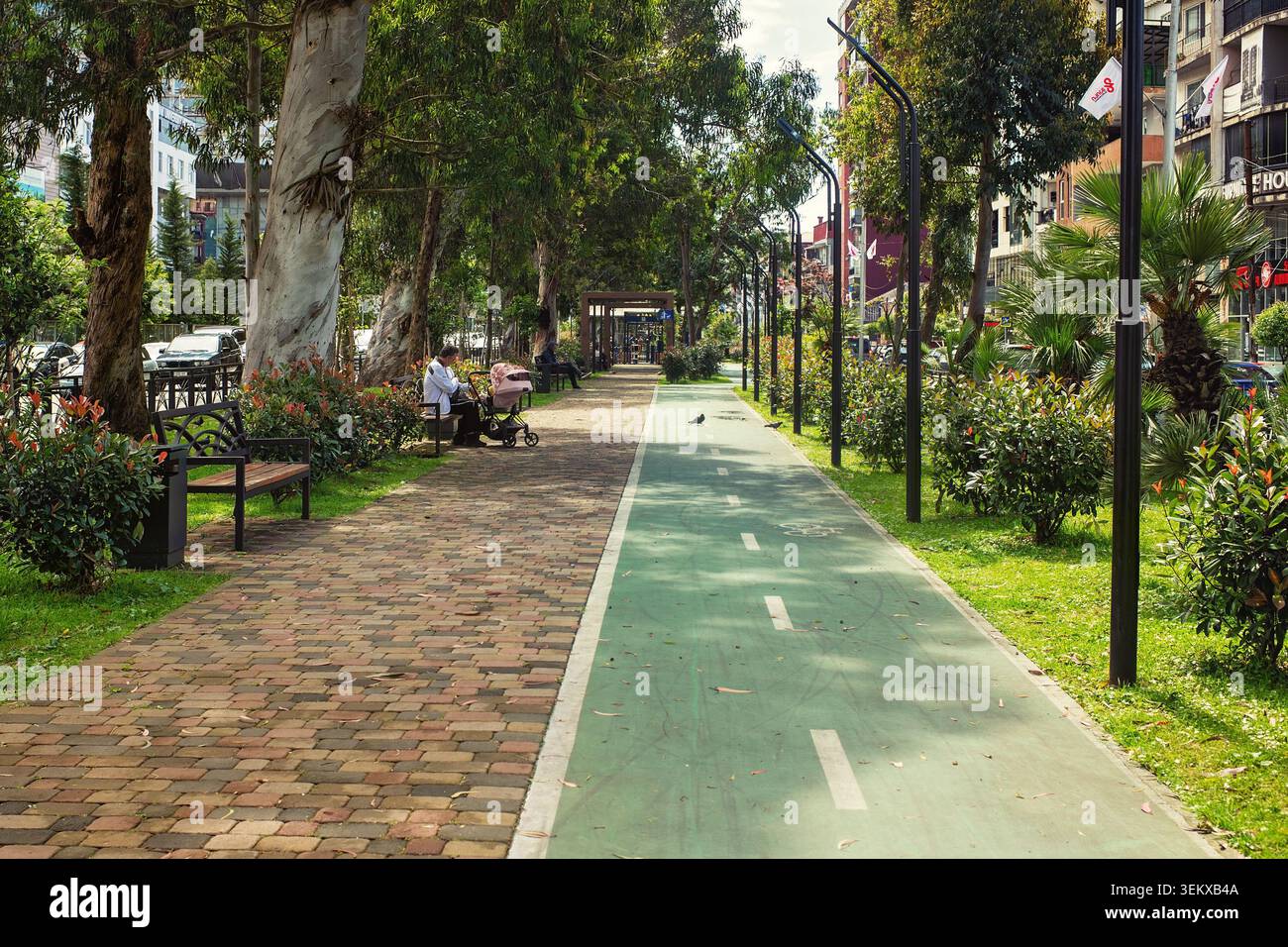 Batumi, Georgia - 30 maggio 2026: Percorso ciclabile verde e passerella pedonale con panchine e alberi lussureggianti su un viale soleggiato della città. Foto Stock