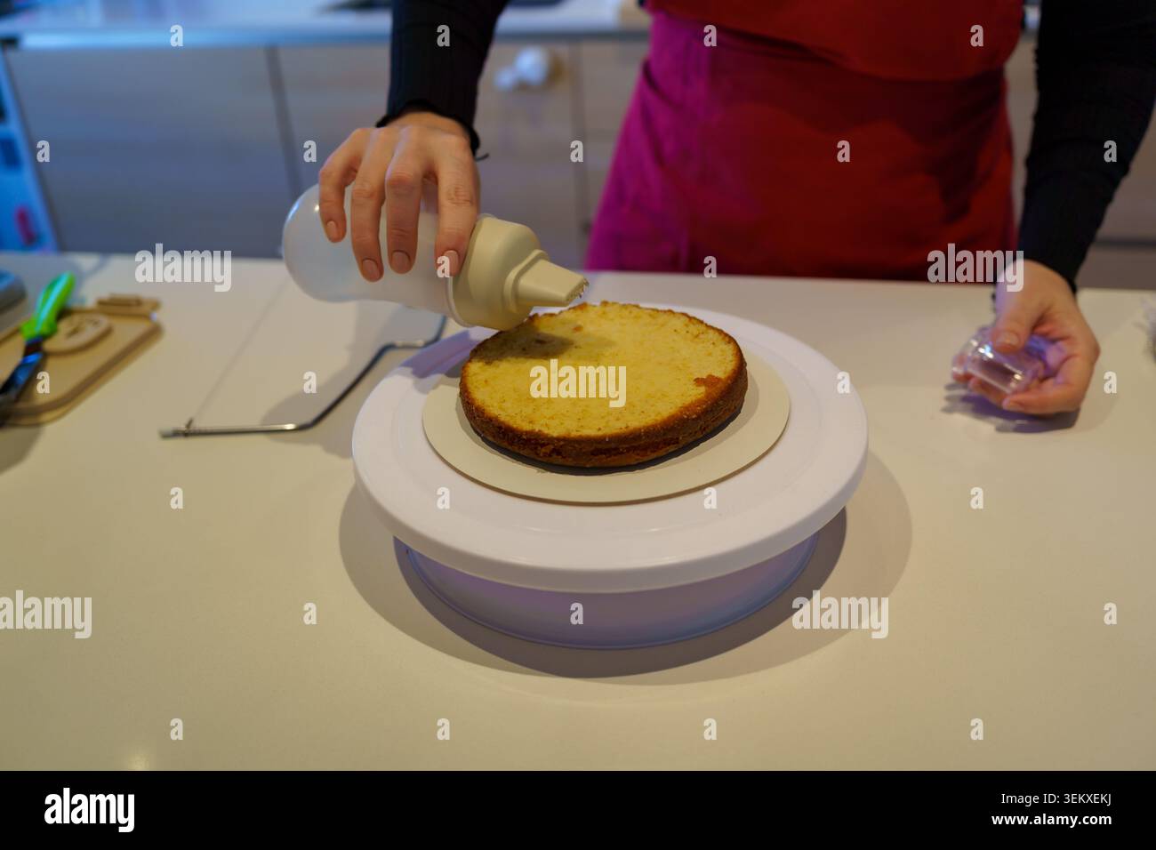 Lo chef inzuppa uno strato di pan di Spagna con sciroppo semplice su un tavolo girevole per torte Foto Stock