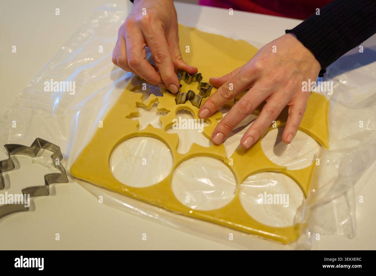 Le mani della persona tagliano fiocchi di neve e forme circolari dall'impasto crudo per biscotti con i taglierini Foto Stock