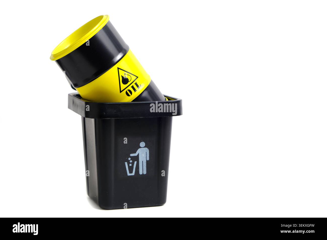 Mini modello di cilindro dell'olio nero e giallo gettato all'interno di un contenitore nero per rifiuti da ufficio su uno spazio bianco Foto Stock
