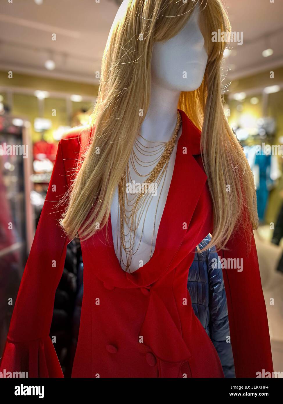Manichino Red Blazer con gioielleria dorata in un ambiente di vendita al dettaglio. Il vivace capo rosso e le collane a strati creano un look accattivante Foto Stock