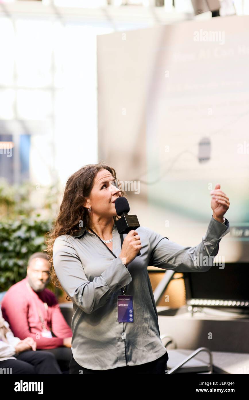 Speaker donna matura che discute i punti di presentazione con il pubblico mentre parla al microfono durante il summit di congr Foto Stock