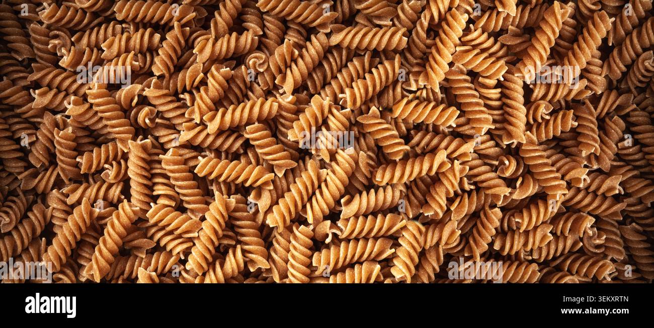 Sfondo texture pasta marrone cruda, motivo fusilli integrale, striscione di tagliatelle a grani interi asciutti, macaroni crudo con spazio di copia per testo, Who Foto Stock