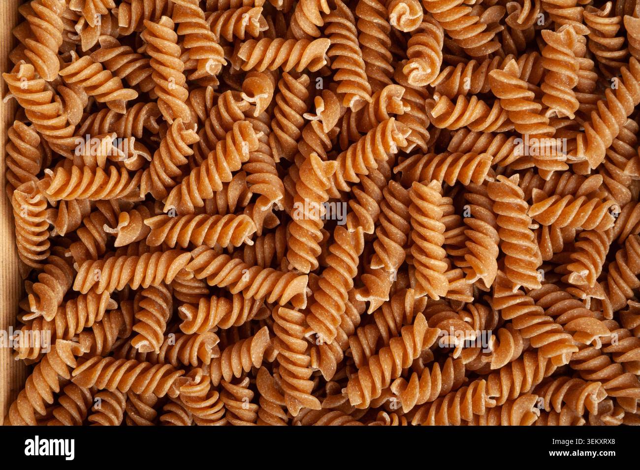 Sfondo texture pasta marrone cruda, motivo fusilli integrale, striscione di tagliatelle a grani interi asciutti, macaroni crudo con spazio di copia per testo, Who Foto Stock