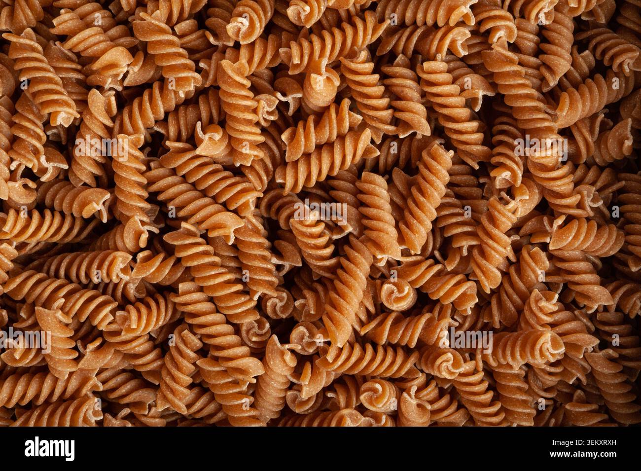 Sfondo texture pasta marrone cruda, motivo fusilli integrale, striscione di tagliatelle a grani interi asciutti, macaroni crudo con spazio di copia per testo, Who Foto Stock