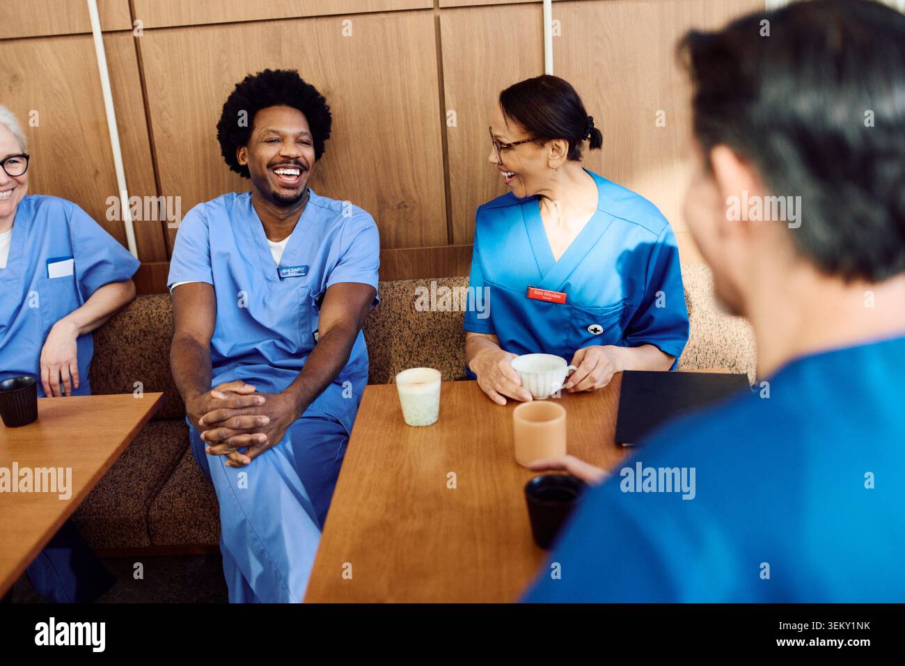 Medico maschio felice godendo di pausa caffè con il team in mensa ospedaliera Foto Stock