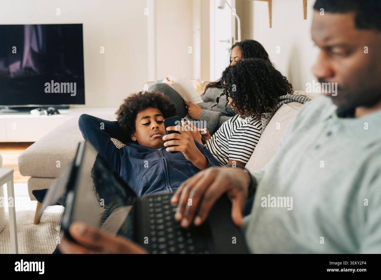 I bambini trascorrono il tempo libero utilizzando gli smartphone mentre si rilassano sul divano con la famiglia a casa Foto Stock