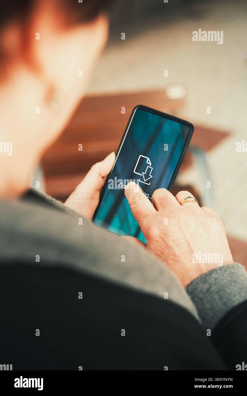 Donna che scarica i file sullo smartphone su schermo di colore verde scuro. Trasferimento di file, aggiornamenti delle app, dati mobili, archiviazione su cloud e produttività digitale. Foto Stock