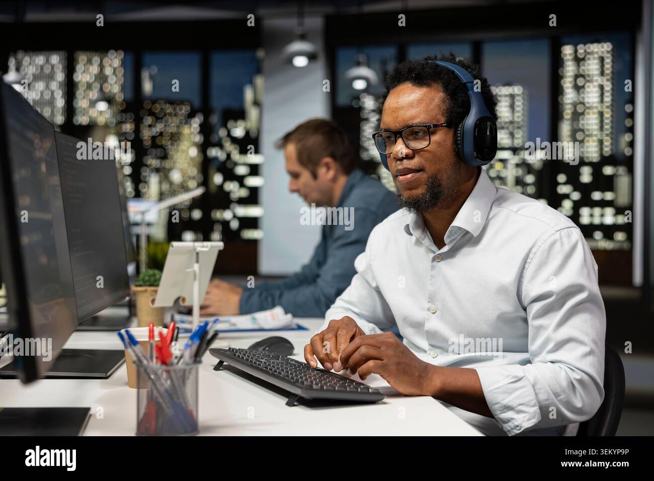 Sviluppatore di software che ascolta musica in ufficio, esamina le metriche di sistema, monitora i dashboard delle prestazioni. Azienda tecnologica esperta IT che mette a disposizione cuffie audio per la sintonizzazione di reti neurali tramite computer Foto Stock