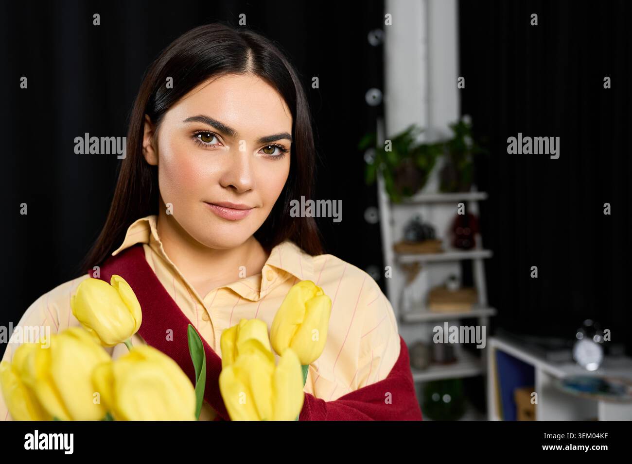Un'affascinante donna sorride calorosamente a casa, cullandosi tra le braccia dei tulipani gialli vibranti. Foto Stock