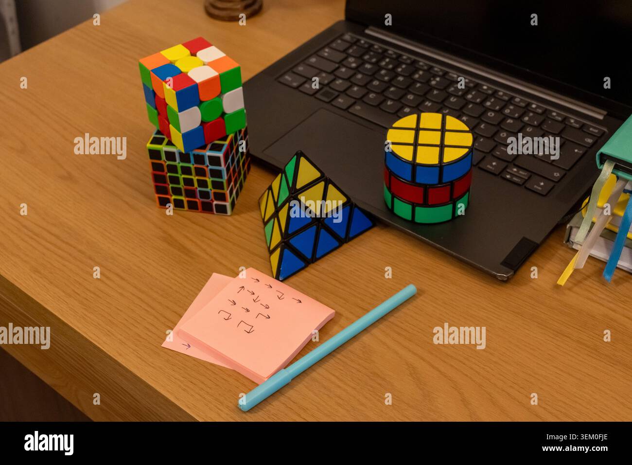 Puzzle logici 3D colorati cubo, piramide e cilindro su una scrivania in legno con laptop, note adesive rosa con frecce e penna. Concetto di pensiero strategico Foto Stock