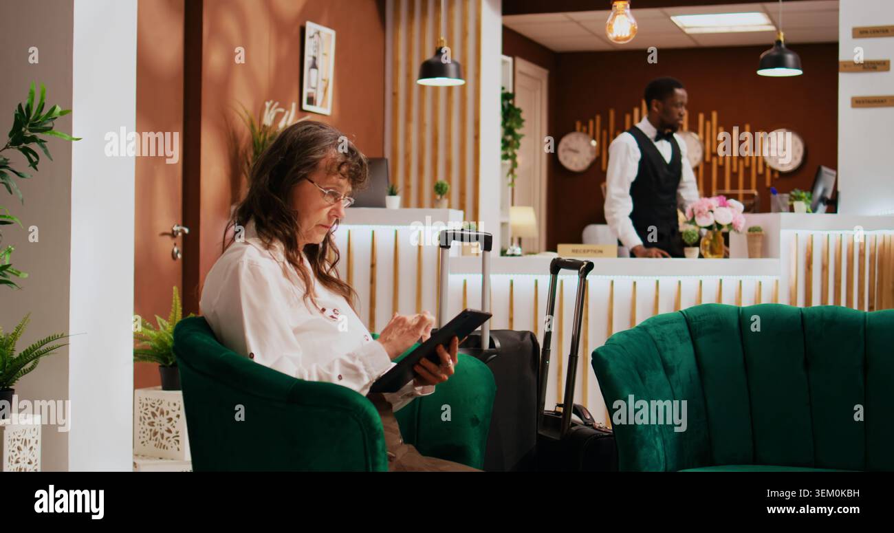 Gli ospiti dell'hotel si rilassano nell'area lounge, utilizzando un tablet moderno per trovare ristoranti e luoghi da visitare. Persone anziane che viaggiano verso il resort all inclusive e aspettano di vedere la camera e iniziare a esplorare. Foto Stock