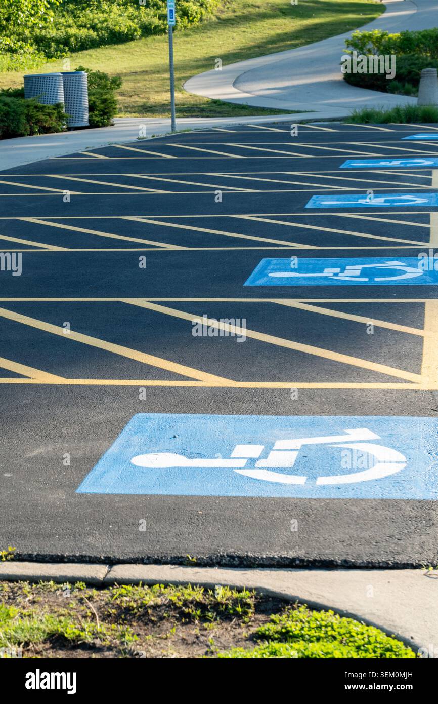 Foto verticale di un parcheggio con più posti auto per disabili contrassegnati con simboli blu per sedie a rotelle sull'asfalto Foto Stock