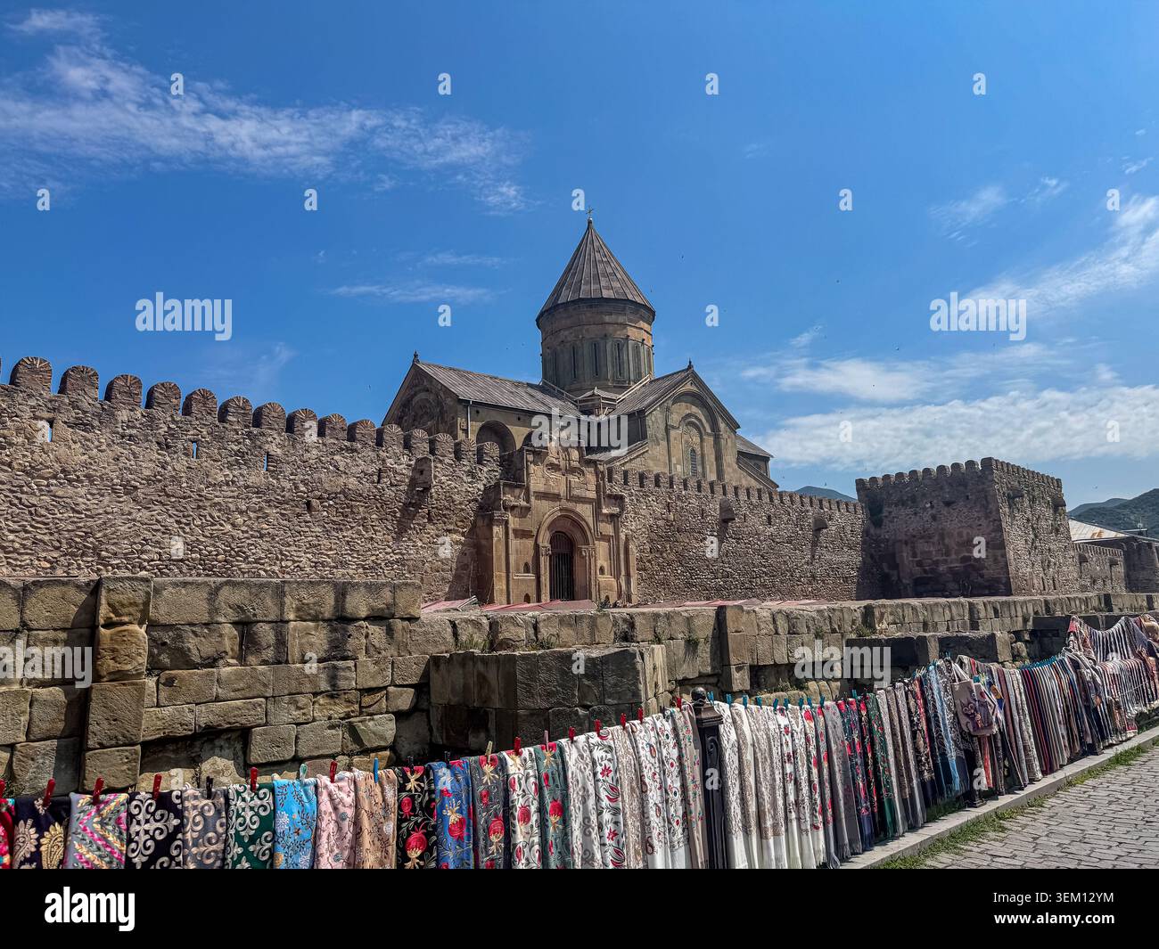 Cattedrale di Svetitskhoveli e mura della fortezza a Mtskheta, Georgia, con tradizionali sciarpe souvenir esposte in vendita in primo piano. - Immagine stock catturata con smartphone