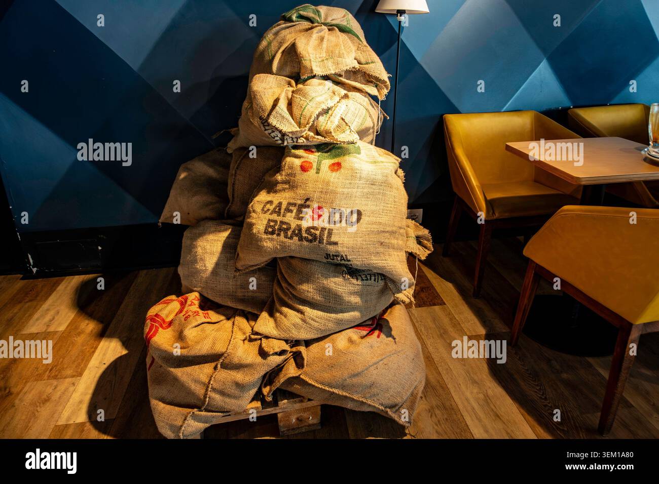 Una pila di sacchi di caffè burlap che leggono "cafés do Brasil" su un pallet di legno all'interno di una moderna caffetteria con sedie gialle a Durrës, Albania. Foto Stock