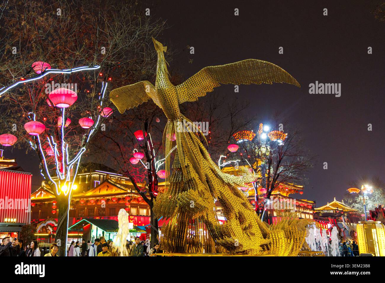 Una scultura dorata di phoenix sorvola le folle tra lanterne rosse e l'architettura illuminata della dinastia Tang a Ever Bright City, Xi'an, Cina Foto Stock