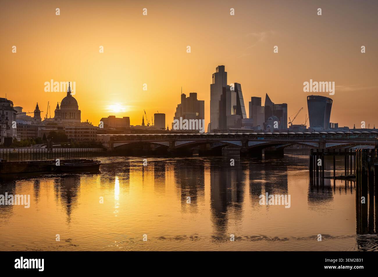 Vista dell'alba estiva d'oro dello skyline della City di Londra, Inghilterra, con riflessi sul Tamigi Foto Stock