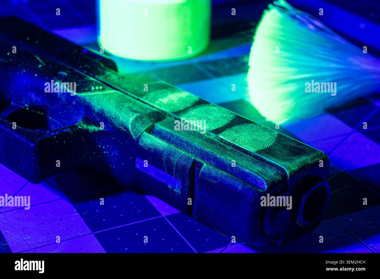 La polvere verde fluorescente delle impronte digitali rivela impronte latenti su una pistola sotto l'illuminazione forense blu, illustrando l'elaborazione delle prove delle armi da fuoco. Foto Stock