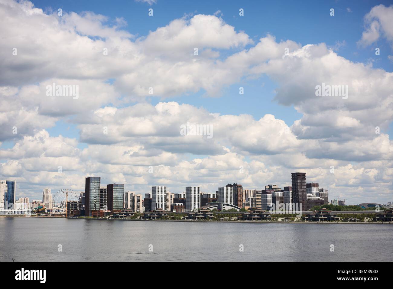 Moderno skyline della città lungo il fiume sotto un cielo blu disseminato di nuvole Foto Stock