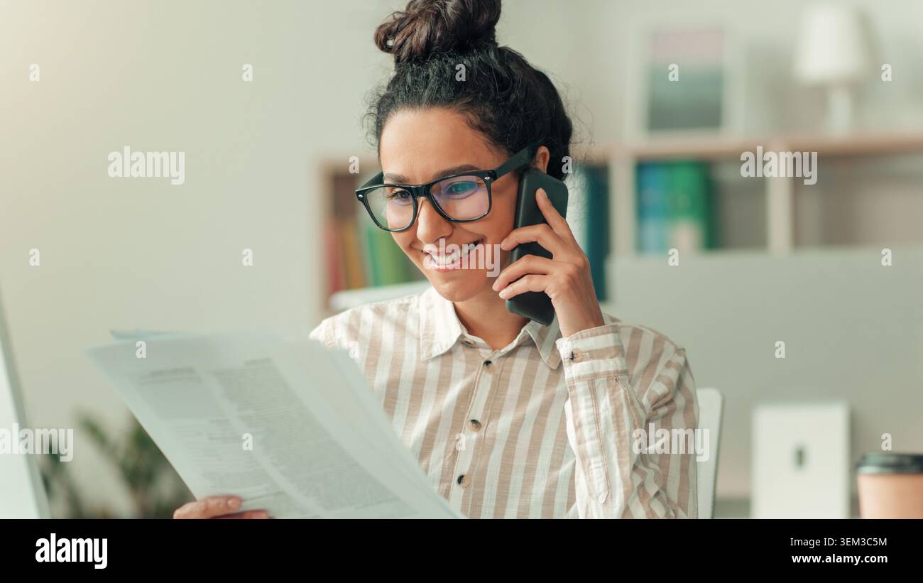 Sorridente giovane donna ispanica che parla sullo smartphone mentre legge documenti in ufficio, concetto di business Foto Stock