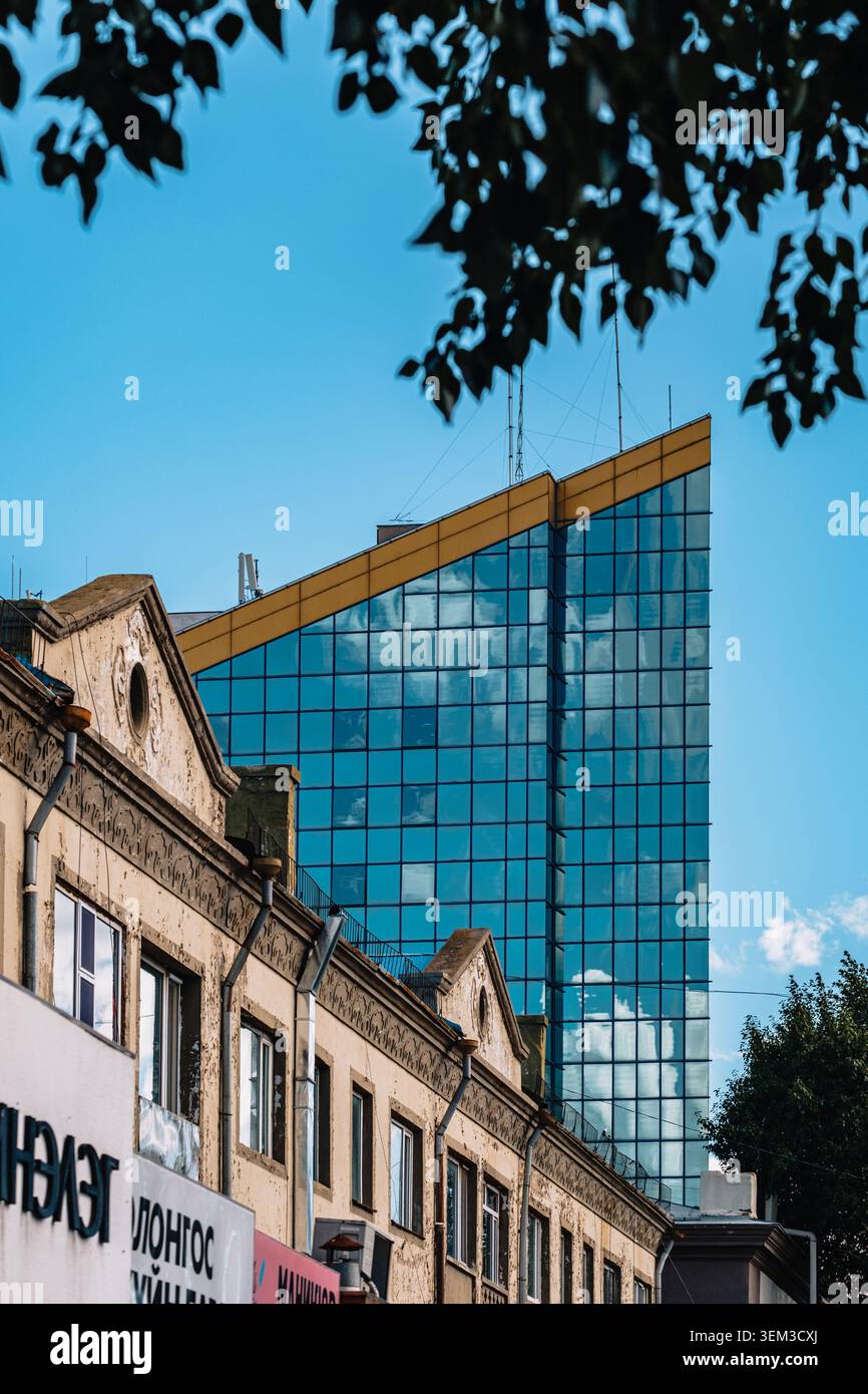 Edifici bassi storici contrastano con una moderna torre di vetro che riflette le nuvole nel centro di Ulaanbaatar, Mongolia. Foto Stock