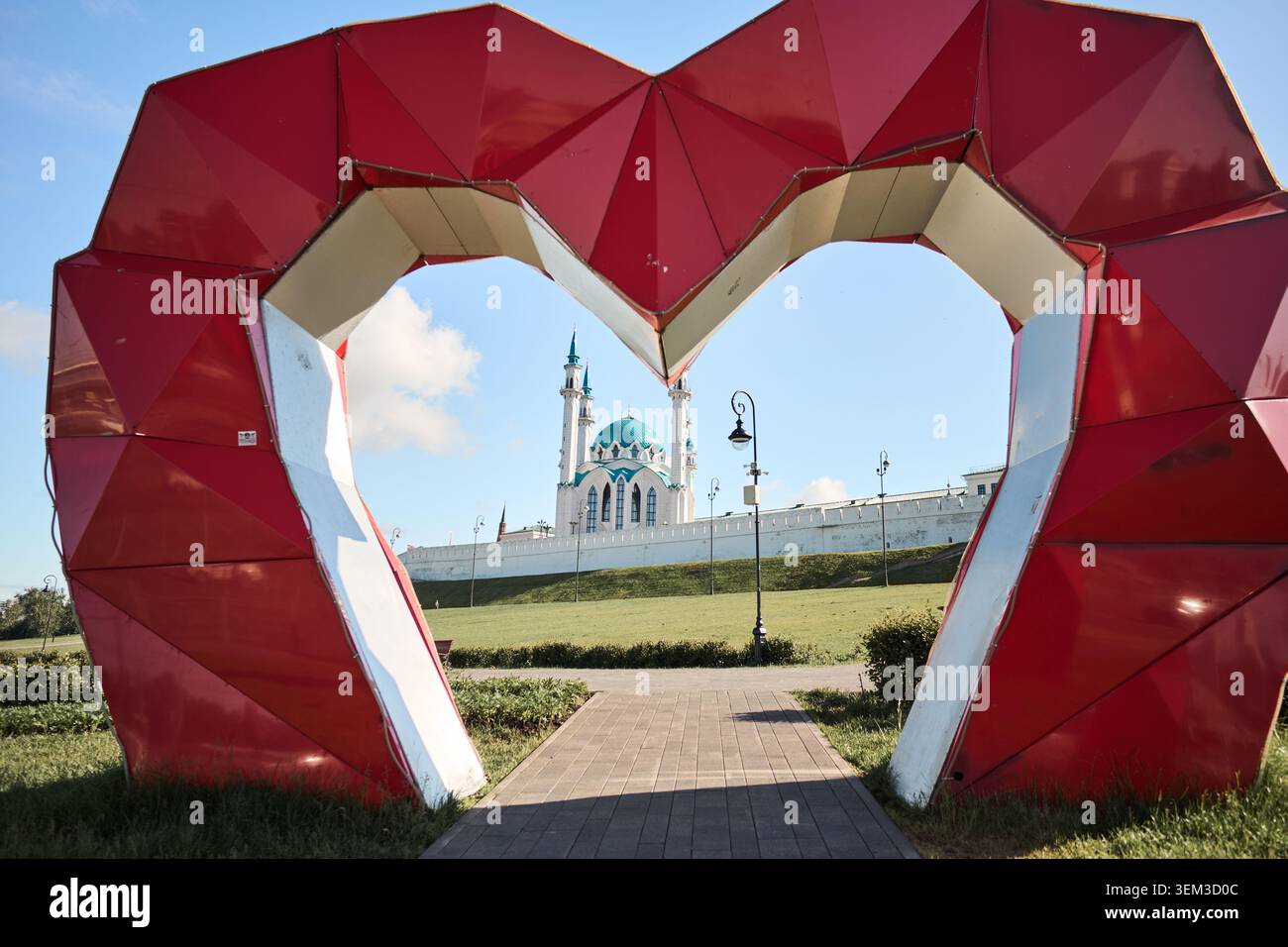 Kazan, Russia - 28.05.2026: Scultura rossa a forma di cuore che incornicia una moschea in una giornata di sole Foto Stock