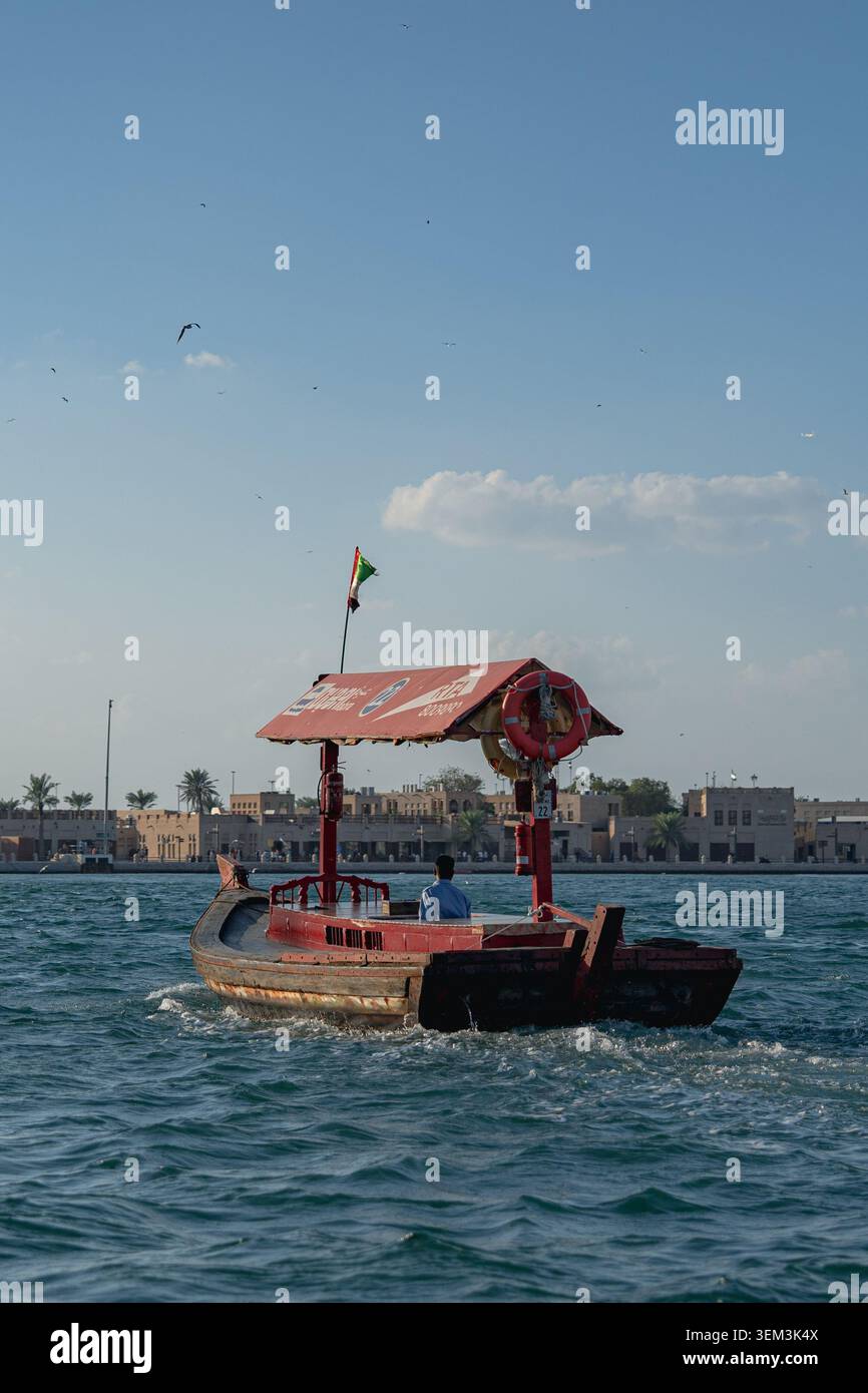 Piccola barca in legno con tetto in barca a vela su un mare blu vicino a una città sul lungomare sotto un cielo limpido Foto Stock