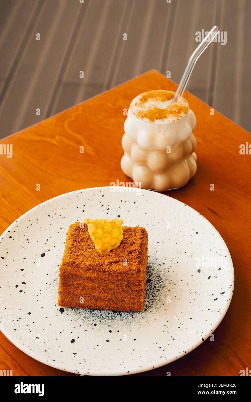 Delizioso dessert servito su un piatto con una bevanda in una caffetteria nel pomeriggio. il dessert quadrato si siede sul piatto accanto al bicchiere di bevanda. tavolo di legno. des Foto Stock