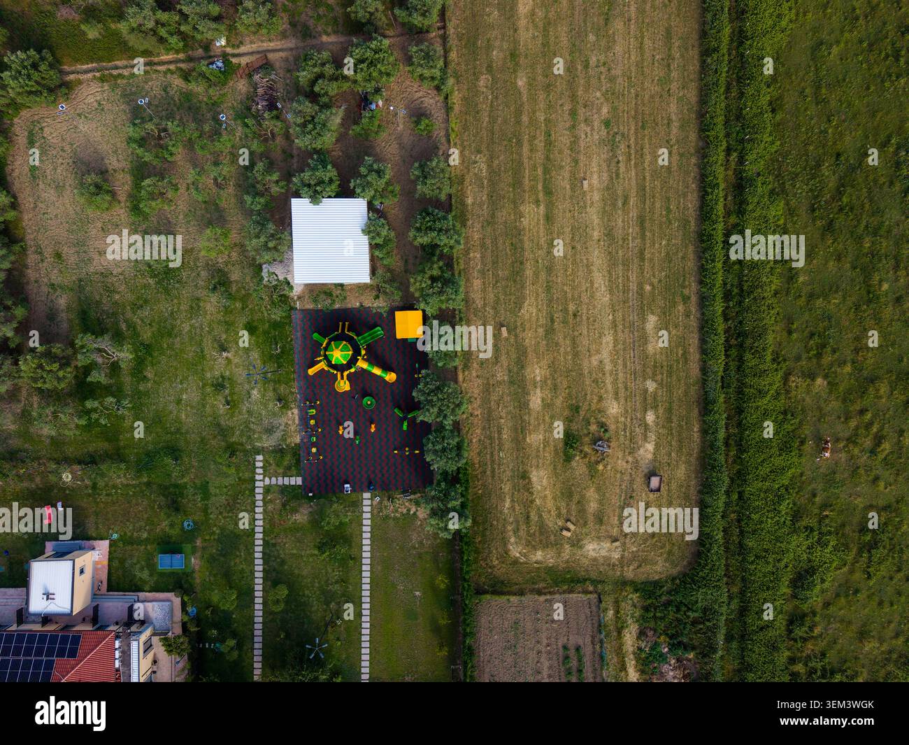 Vista aerea di un colorato parco giochi per bambini con scivoli gialli accanto a un edificio bianco e lussureggianti campi verdi di Zvernec, Vlore County, Albania. Foto Stock