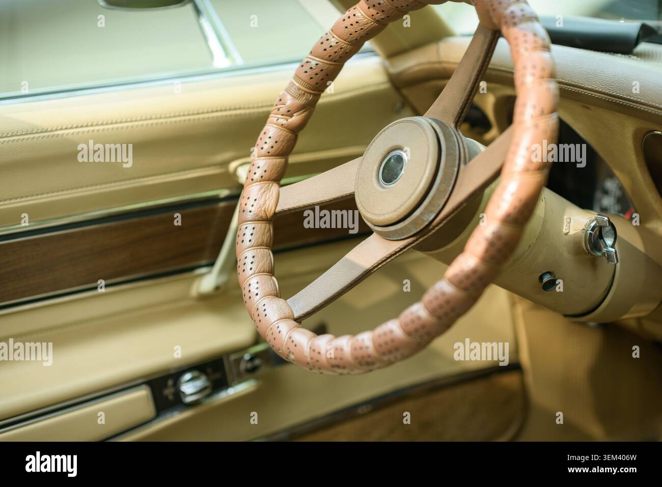 Il volante di un'auto d'epoca e il cruscotto beige sono mostrati all'interno di un abitacolo classico dopo la rimozione del marchio visibile. Foto Stock