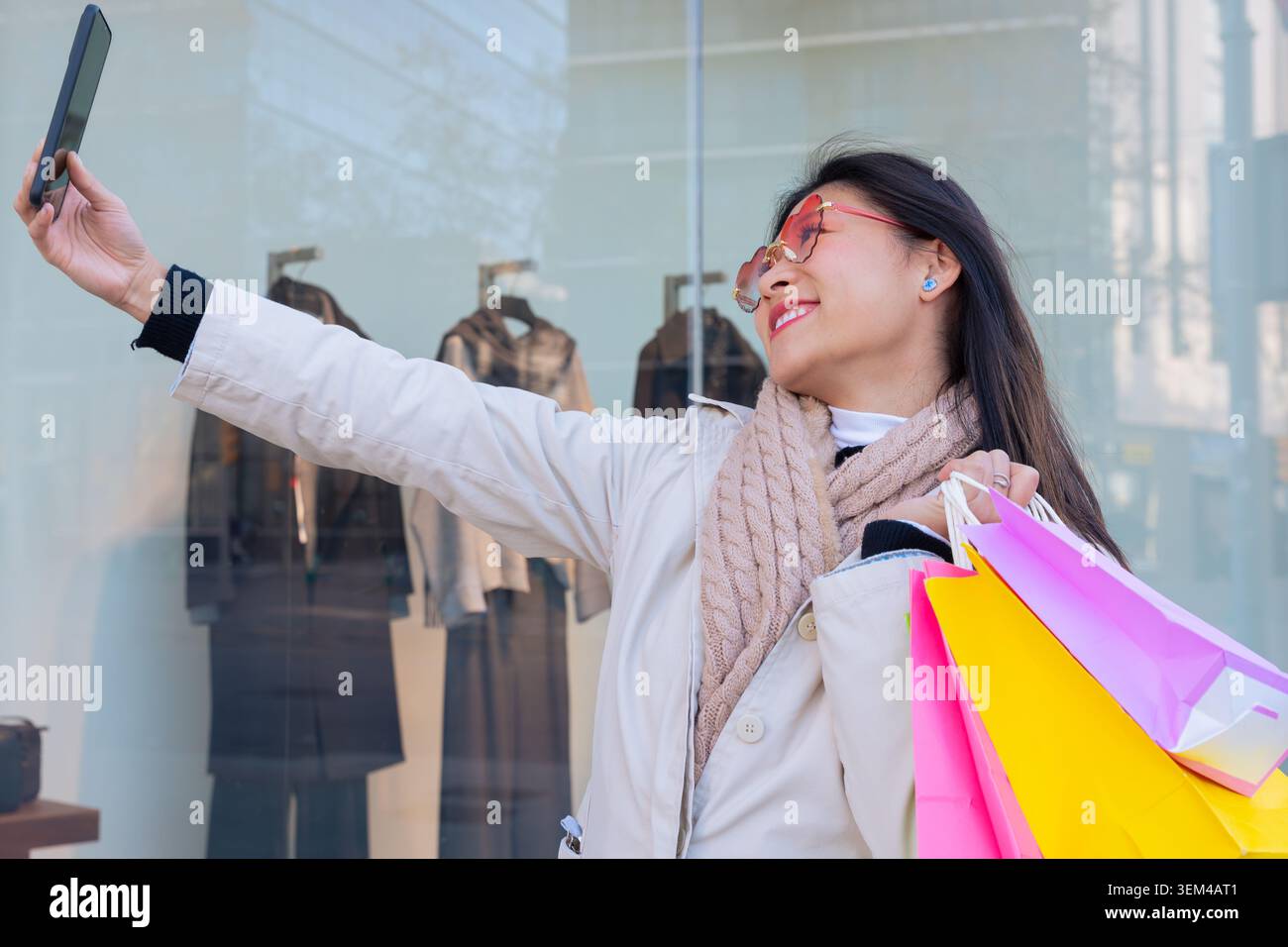 Donna sorridente che tiene in mano le borse della spesa scattando un selfie con il suo smartphone all'aperto. Foto Stock