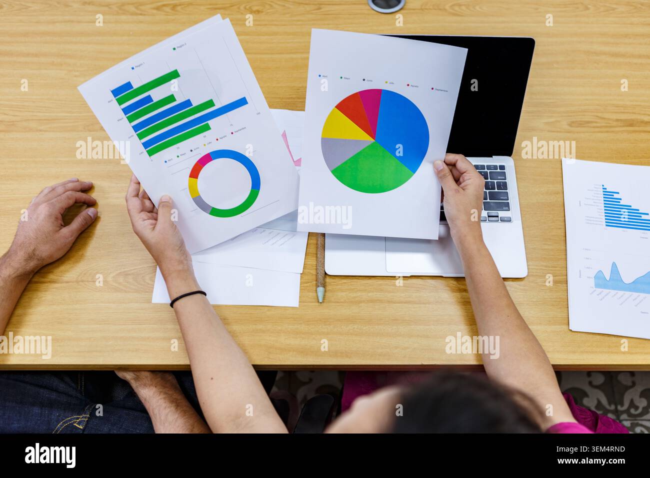Due persone stanno esaminando i rapporti finanziari e i grafici in uno spazio di coworking. L'analisi avviene durante una sessione di lavoro su una scrivania condivisa. Questo Foto Stock