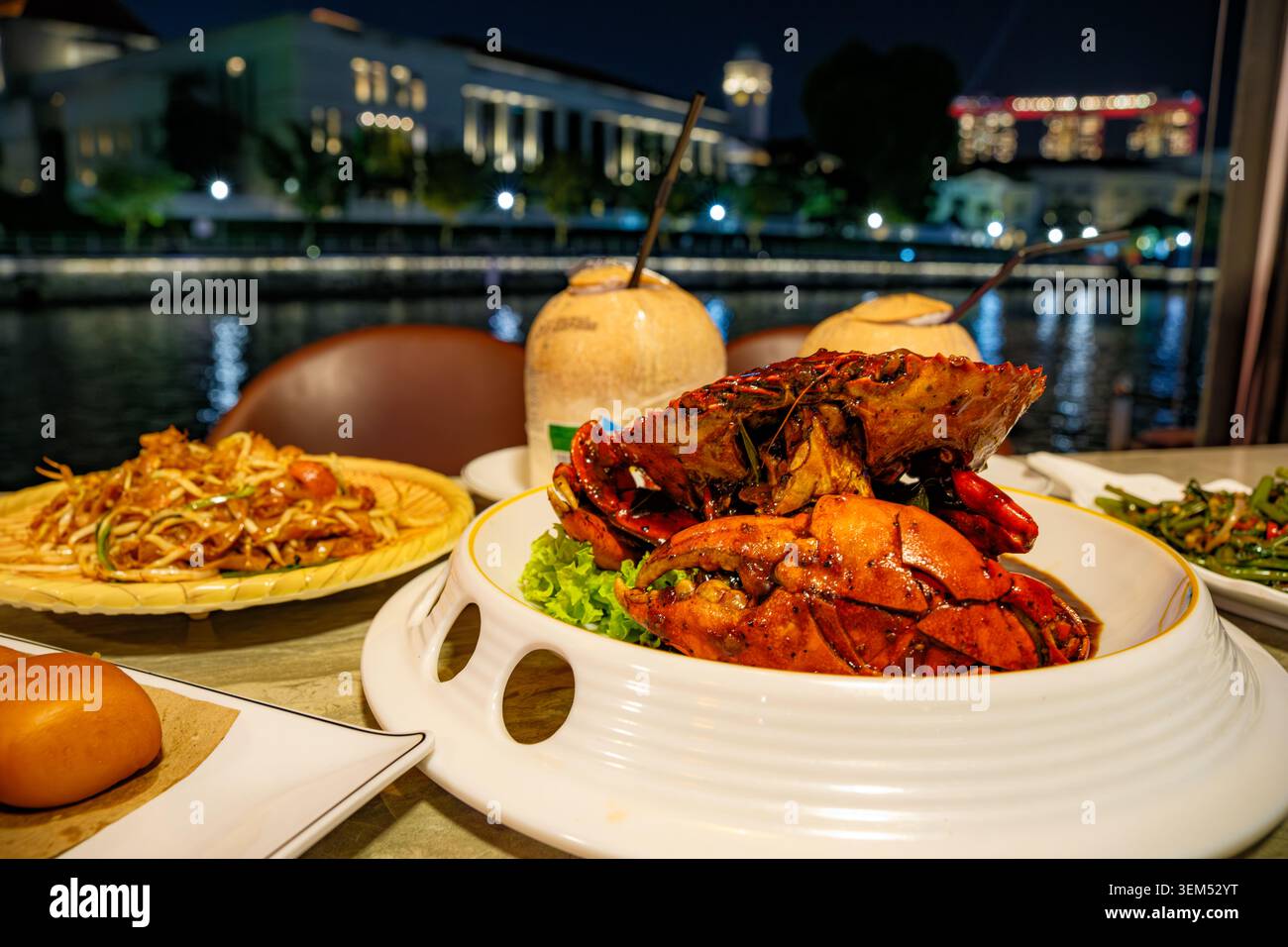 Fotografia gastronomica professionale che raffigura l'iconico granchio di Singapore su un piatto bianco con noci di cocco fresche in un ristorante notturno sul fiume. P Foto Stock