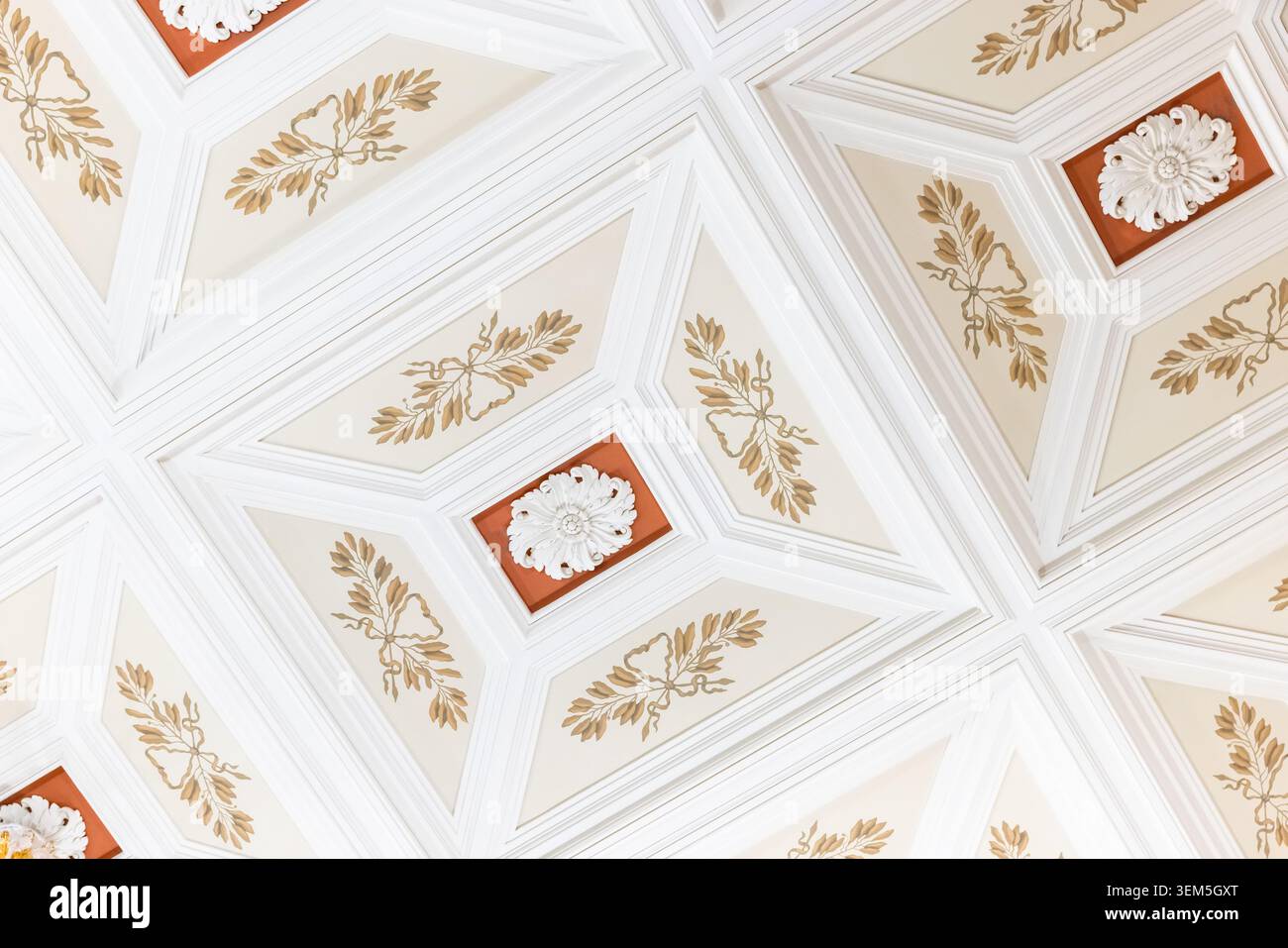 Elegante soffitto a cassettoni con pannelli geometrici, foglie dorate e rosette in gesso. Le tonalità di crema e terracotta mettono in risalto i clas Foto Stock