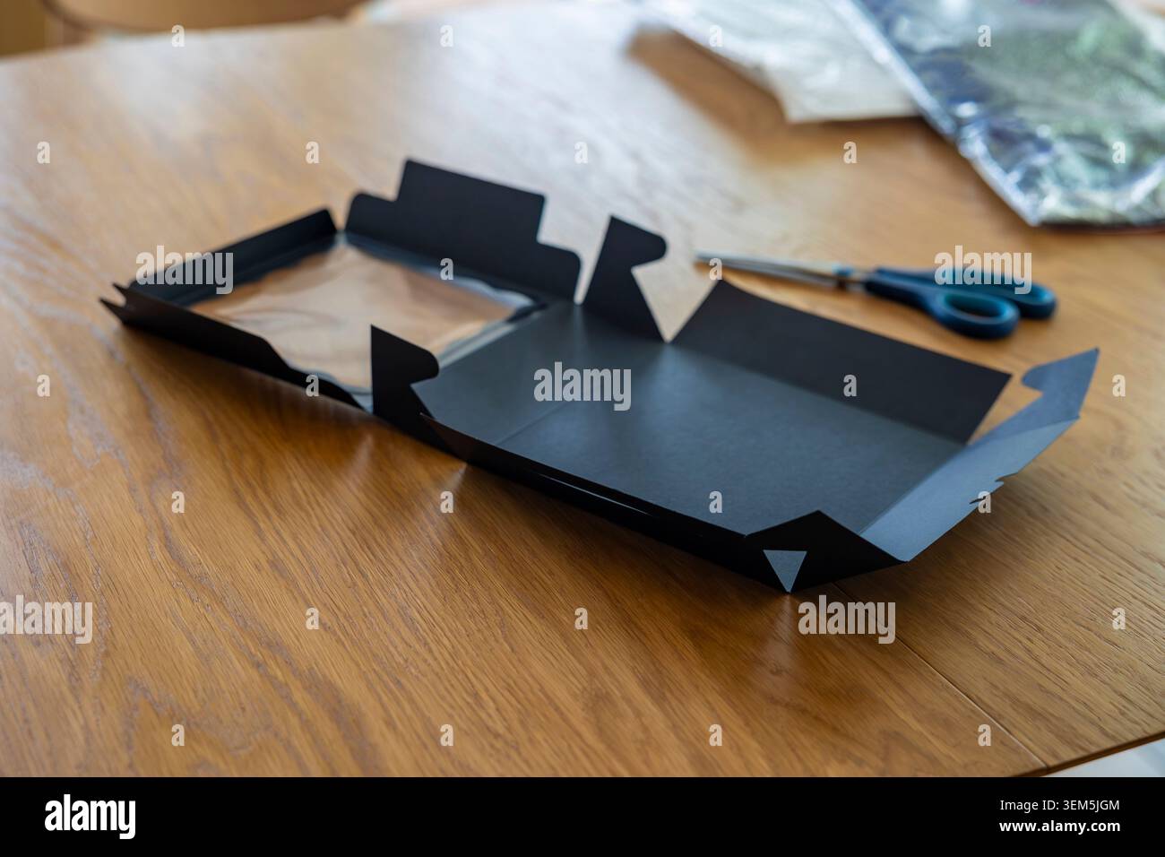 Confezione regalo in cartone nero opaco su un tavolo in legno alla luce del sole con forbici blu. Concetto: Imballaggio e-commerce Foto Stock